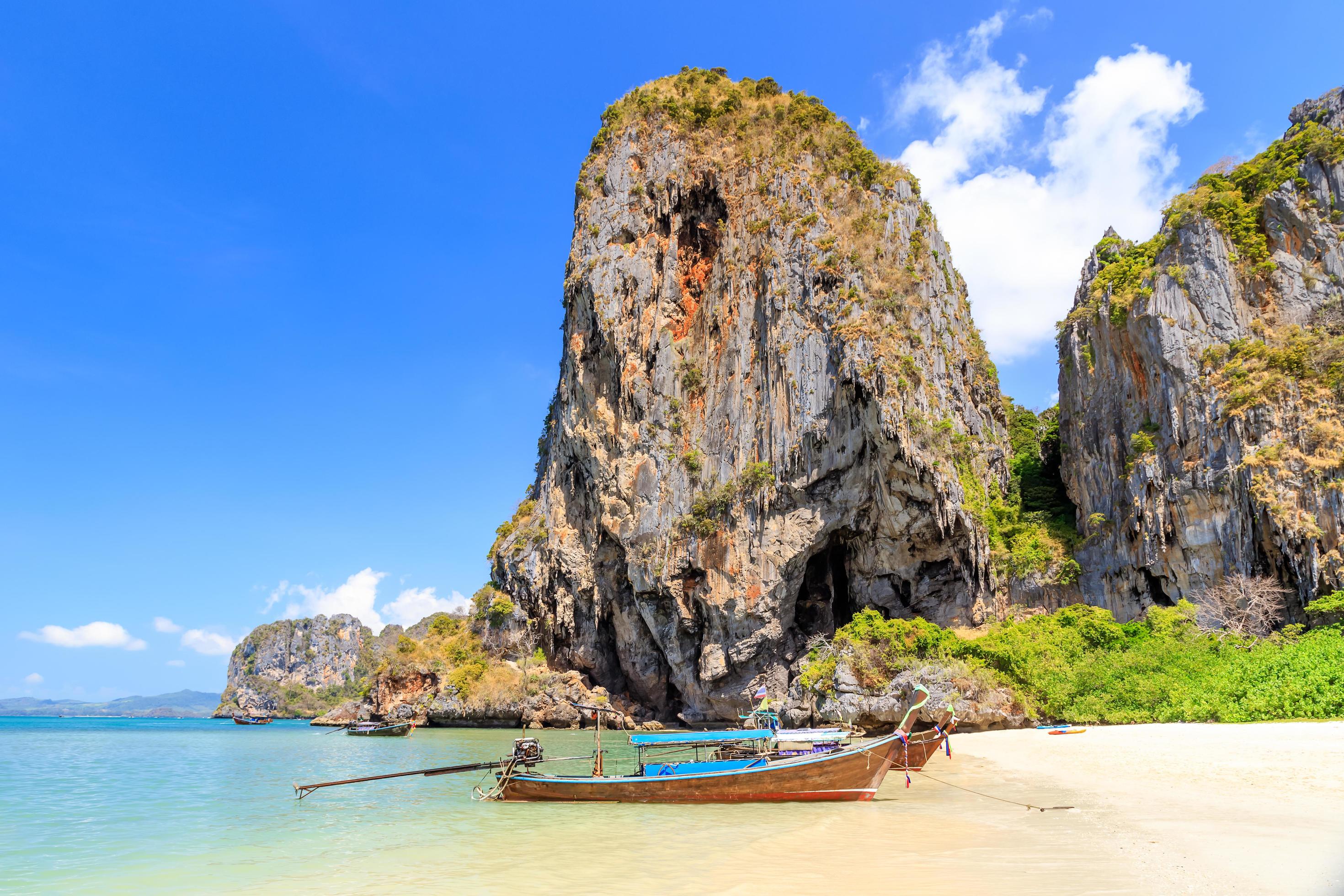 A long-tail boat beside limestone cliffs and clear water in Krabi, Thailand